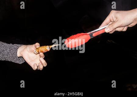 Hand mit roter Zange reicht eine gekochte Krabbenkralle an die Hand einer anderen Frau, die sie in den Fingern hält - ohne Keime zu teilen Stockfoto