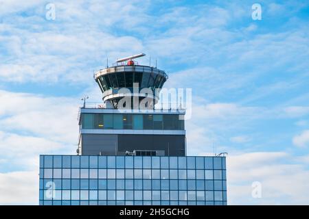 Funktionierender Flughafenkontrollturm mit transparenter Kabine. Lufttransport-Kommandoposten auf mehrstöckigen Gebäude oben, blauer Himmel Licht Wolken Hintergrund Stockfoto