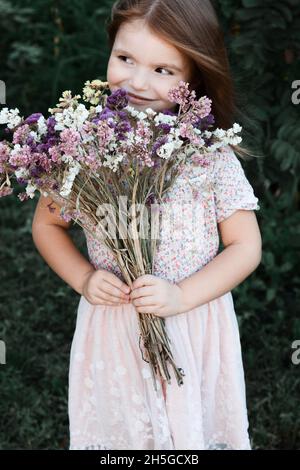 Kleines Mädchen mit Blumen, gelbe Blumen Sonnenblume, sammelt Blumen im Garten, niedliches Kind 5 Jahre alt Stockfoto