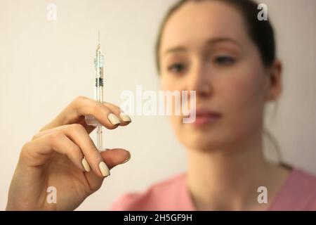 Krankenschwester, Kosmetikerin in einem rosa medizinischen Kleid, die eine Spritze mit einer dünnen Nadel in der Hand hält. Beauty-Injektionen, Kosmetologie. Gesundheitswesen, Medizin. Beau Stockfoto