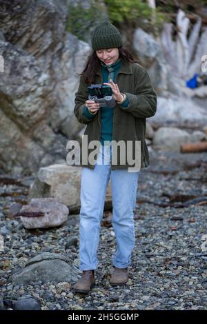 Junge Frau steht mit der Fernbedienung für eine Drohne im Whytecliff Park, Horseshoe Bay; British Columbia, Kanada Stockfoto