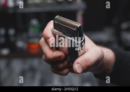 Die Hand eines Friseurs oder Friseurs hält einen automatischen Haarschneider zum Schneiden und Rasieren von Nahaufnahme vor dem Hintergrund des Salons. Stockfoto