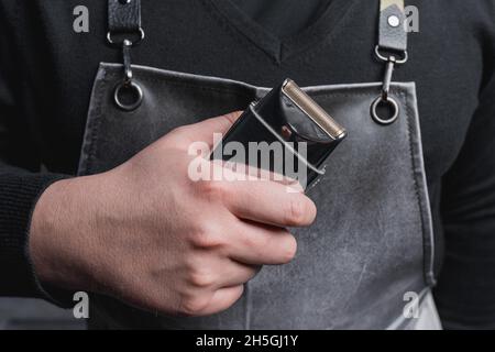 Die Hand eines Friseurs oder Friseurs hält einen automatischen Haarschneider zum Schneiden und Rasieren von Nahaufnahme vor dem Hintergrund des Salons. Stockfoto