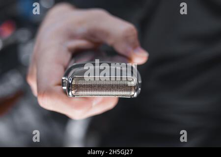 Die Hand eines Friseurs oder Friseurs hält einen automatischen Haarschneider zum Schneiden und Rasieren von Nahaufnahme vor dem Hintergrund des Salons. Stockfoto