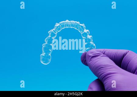 Hand hält einen transparenten Halter auf blauem Hintergrund. Invisalign Kieferorthopädie Konzept Stockfoto