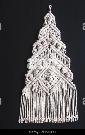 Weihnachtsbaum Ornament Makrame aus weißen Naturbaumwollfäden auf schwarzem Hintergrund. Festlicher weihnachtsbaum, geflochten aus Garn auf dunklem Hintergrund Stockfoto