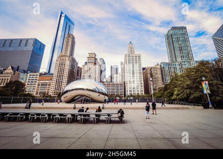 Menschen sitzen auf Bänken vor Sir Anish Kapoors Skulptur Cloud Gate, die den Spitznamen The Bean trägt, vor der Skyline von Chicago, IL, USA Stockfoto