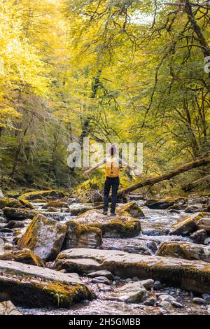 Junge Wanderin, die in einem fließenden Fluss in Passerelle d'Holzarte in Larrau, Frankreich, auf Felsen läuft Stockfoto