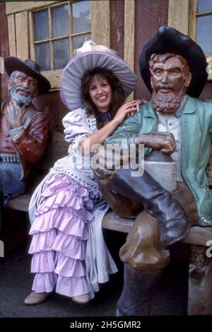 Frau im historischen Kostüm posiert mit holzgeschnitzten Figuren von Männern aus der Wild-West-Zeit im Knott's Vergnügungspark in Buena Park, CA Stockfoto