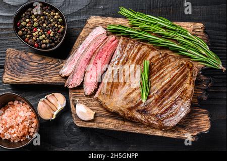 BBQ gegrillte Flanke oder Lasche Rindersteak auf einem hölzernen Schneidebrett. Schwarzer Holzhintergrund. Draufsicht Stockfoto