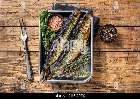 Geräucherter marinierter Heringfisch in Küchentablett mit Kräutern. Holzhintergrund. Draufsicht Stockfoto