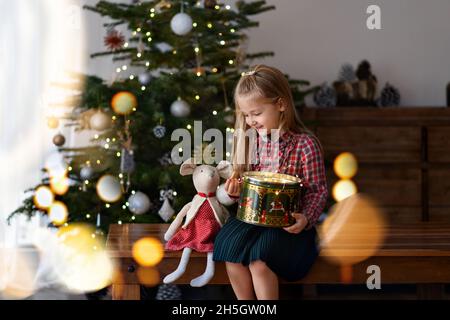 Mädchen mit einem Geschenk sitzt in der Nähe des Weihnachtsbaums Stockfoto