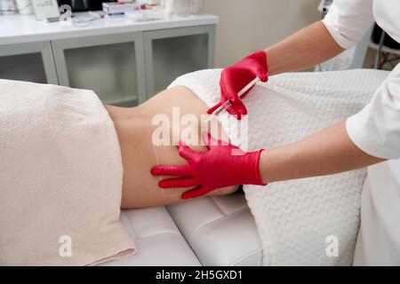 Junge Frau bekommt fettreduktive Haut Lifting Körperbehandlung durch einen Kosmetologen. Attraktive weibliche Patientin, die sich gerne an schlankeren Körperkonturierung erfreut Stockfoto