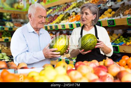 Dame im Gemüsehändler hilft dem alten Mann, Melone zu wählen Stockfoto