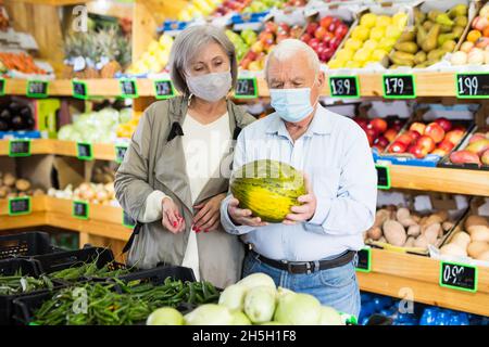 Ehepaar in Schutzmaske kaufen reife Wassermelone im Supermarkt Stockfoto