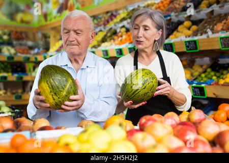 Dame im Gemüsehändler hilft dem alten Mann, Melone zu wählen Stockfoto