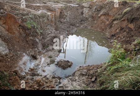Tiefes Loch mit Wasser nach dem Graben für die Installation neuer Wasserleitungen Stockfoto