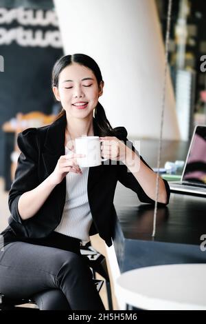 Eine Marketingmanagerin ruht sich mit einer Tasse Kaffee aus, bevor sie zur Arbeit zurückkehrt, um Schläfrigkeit zu reduzieren. Stockfoto