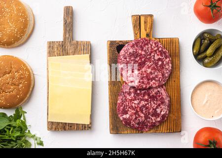 Hausgemachter Hamburger. Hacksteaks, Sesambrötchen mit anderen Zutaten, auf weißem Steingrund, Draufsicht flach liegend Stockfoto