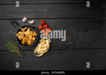 Rohe Tagliatelle mit Zutaten für Pfifferlinge, auf schwarzem Holztischhintergrund, Draufsicht flach liegend, mit Platz für Text Stockfoto