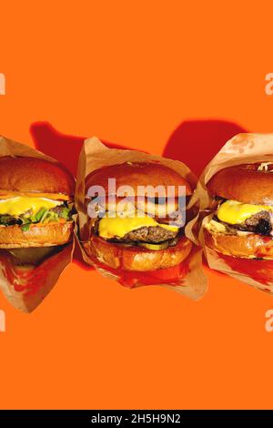 Drei verschiedene Burger in einer Packung auf einem leuchtend orangefarbenen Hintergrund. Schnelle Lieferung von Lebensmitteln. Draufsicht. Stockfoto