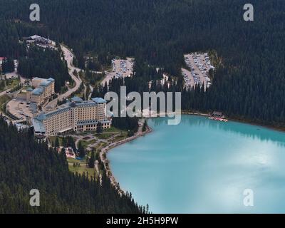 Blick auf den östlichen Lake Louise mit türkisfarbenem Wasser, berühmtes Hotel und Parkplatz, umgeben von Wäldern im Banff National Park, Kanada. Stockfoto