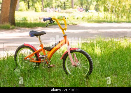 Auf dem grünen Gras steht ein rotes Kinderfahrrad Stockfoto