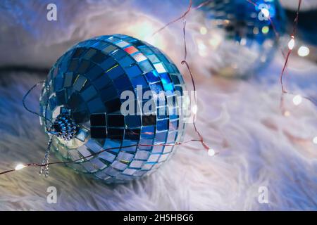 Zwei Diskokugeln liegen auf einer gemütlichen Decke mit weihnachtlicher Girlande-Beleuchtung. Gemütliche Innenausstattung. Home Sweet Home. Nach der Party. Dekoration zum neuen Jahr. Stockfoto