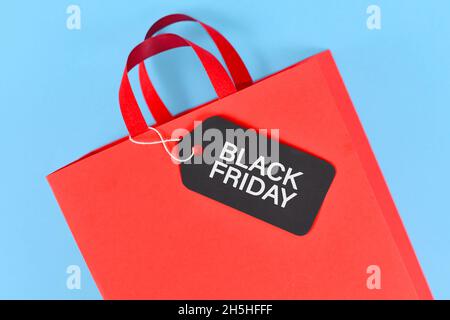 Schwarzes Freitagsetikett auf roter Papier-Einkaufstasche auf blauem Hintergrund Stockfoto