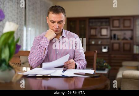 Trauriger frustriert Mann Blick auf Papier, die am Tisch sitzen Stockfoto