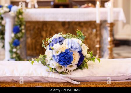 Farbenfroher Brautstrauß aus weißen und blauen Blumen, der auf Kissen über der Hochzeitsbank vor dem Kirchenaltar liegt Stockfoto