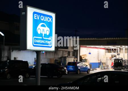 EV Schnellladestelle für Elektrofahrzeuge. Blaues Leuchtzeichen. Werkstatt im Hintergrund. Stockfoto