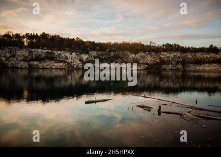 Rock cliffs with autumn trees atop reflecting in calm water at sunset, Artificial water reservoir, former limestone quarry in Krakow, Poland Stock Photo