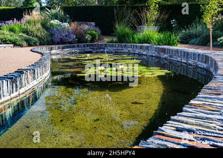 Farbenfrohe, flache Ansicht des größten Wasserspiegels im Cool Garden von RHS Rosemoor mit Lilys, Reflections und Naturstein-Details. Stockfoto