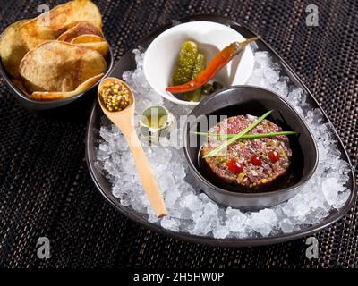 Gourmet-Rindertartare serviert auf zerstoßenem Eis mit Gurken, Senf, Wachteleiergelb und Toastchips Stockfoto