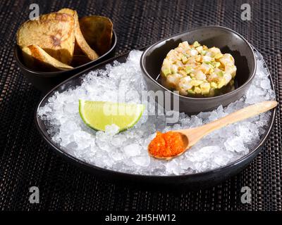 Gourmet-Fisch-Tatar mit Avocado, serviert auf zerstoßenem Eis mit rotem Kaviar, Limette und knusprigen Toasts Stockfoto