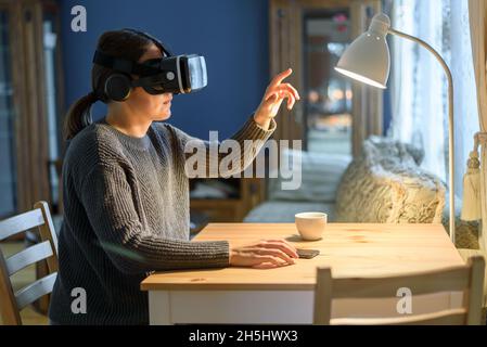 Frau in Strickpullover mit vr Virtual Reality-Headset im Wohnzimmer. Für Arbeit oder Unterhaltung Stockfoto
