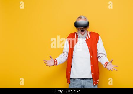 Schockierter Mann mittleren Alters in Bomberjacke und vr-Headset auf Gelb Stockfoto
