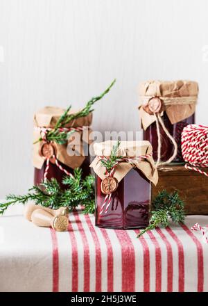 Handgemachtes Geschenk zu Weihnachten. Hausgemachte Obstkonfitüre in den mit Grunge-Papier, Wachssiegel und grünem Zweig von Nadelbäumen verzierten Gläsern. Stockfoto