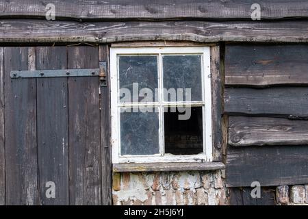 Blick auf verwitterte Türen, Fenster und Stallbretter verfallener und verlassener Stallungen auf einem Bauernhof auf dem Land in den Niederlanden Stockfoto