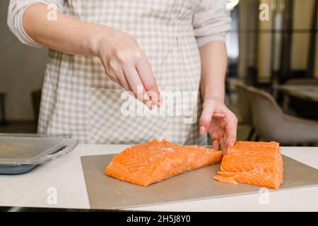 Frau salzt rotes Fischfilet. Leicht gesalzener Lachs wird vorbereitet. Stockfoto