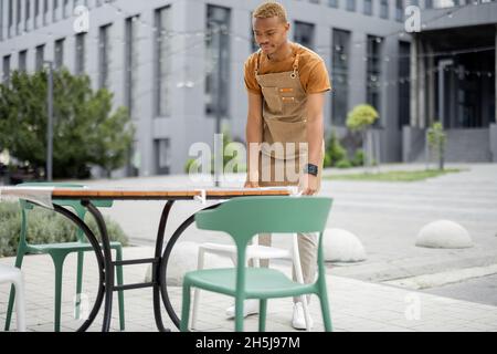 Der Kellner korrigierte den Stuhl am Tisch im Café im Freien Stockfoto