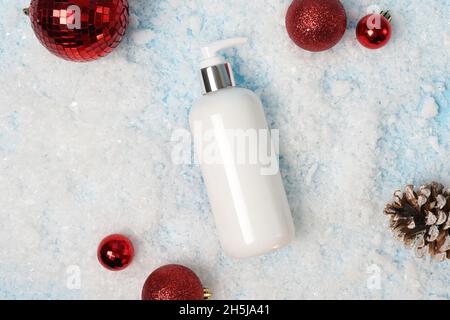 Kosmetische Produkt Lotion oder Shampoo auf weißem weihnachtshintergrund mit Schnee und roten Dekorationen, flach legen. Winterpflege Stockfoto