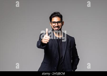 Porträt eines glücklichen zufriedenen, gut aussehenden bärtigen Geschäftsmanns mit Daumen nach oben auf grauem Hintergrund. Stockfoto