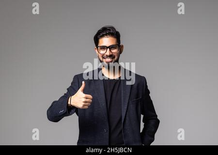 Porträt eines glücklichen zufriedenen, gut aussehenden bärtigen Geschäftsmanns mit Daumen nach oben auf grauem Hintergrund. Stockfoto