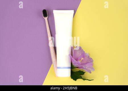Tube Zahnpasta mit einer Zahnbürste aus recyceltem Kunststoff mit violetter Blume auf farbigem Hintergrund. Eco Consumption Konzept Stockfoto