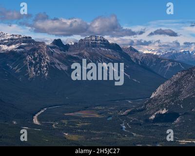 Blick über die Rocky Mountains (riesige Bergkette) mit schneebedeckten Gipfeln über dem Bow Valley mit Wäldern, gewundenem Bach und Trans-Canada Highway. Stockfoto