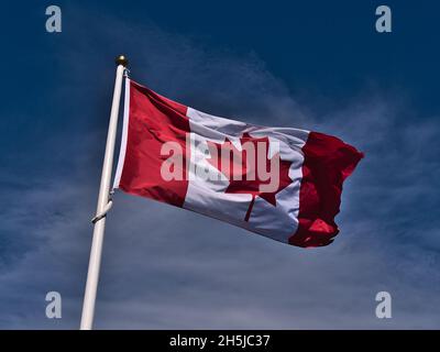 Niedrige Ansicht der fliegenden kanadischen Nationalflagge mit weißen und roten Farben und Ahornblatt in der Mitte auf Fahnenmast vor blauem Himmel mit Wolken. Stockfoto