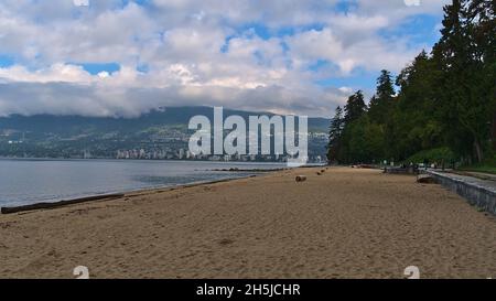 Schöner Blick auf den sandigen Third Beach im Stanley Park, Vancouver, British Columbia, Kanada am Morgen mit Bäumen und Menschen vorbei und Stadt. Stockfoto