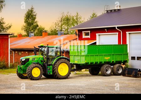 John Deere 6155R Traktor vor dem Palmse 1900 Anhänger auf dem Hof im Morgenlicht. Salo, Finnland. 29. August 2020. Stockfoto